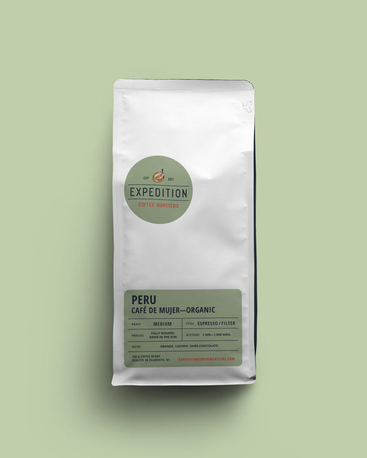 A white bag of Expedition Coffee Roasters 'Peru Cafe de Mujer-Organic' coffee beans, centered on a solid sage green background.